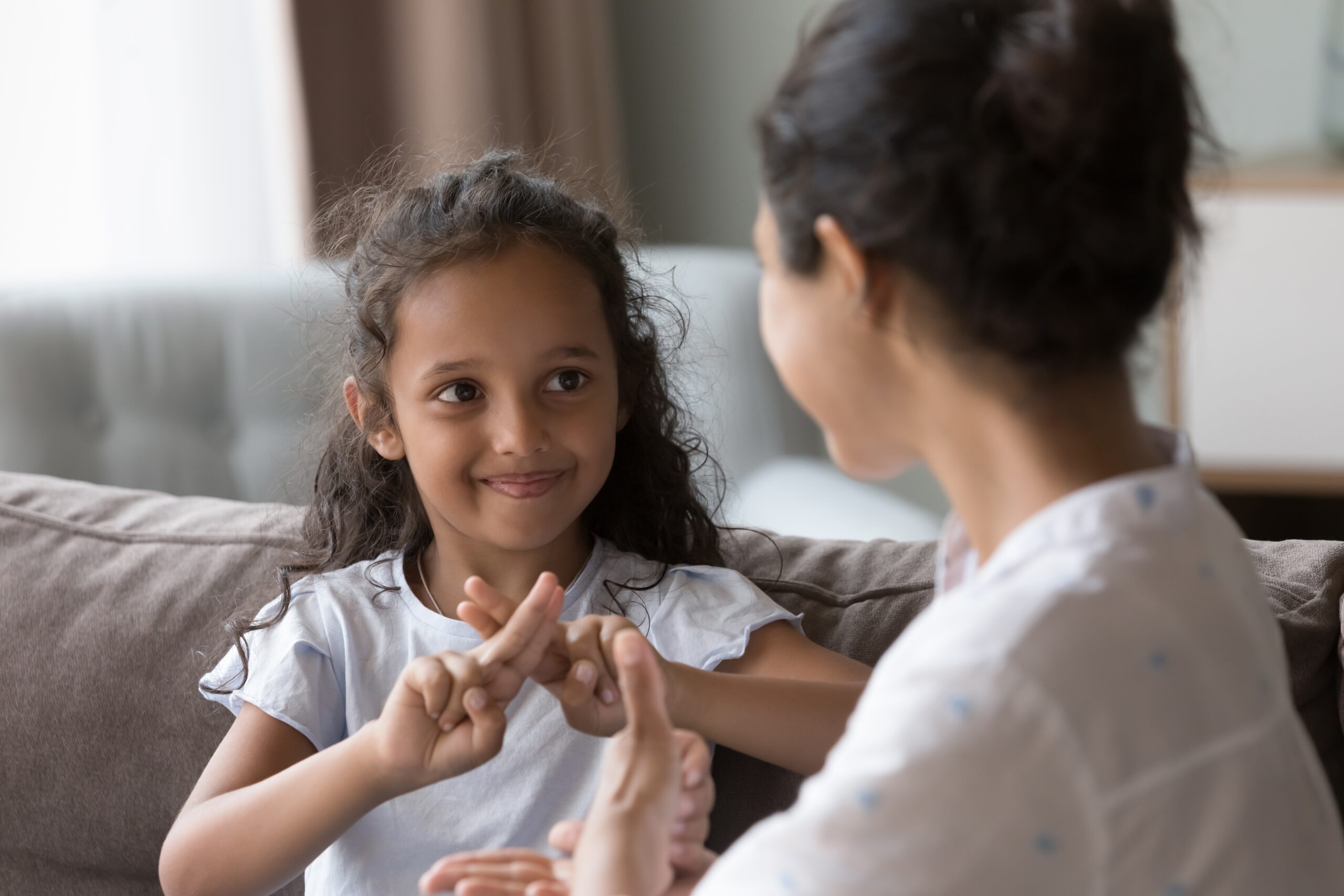 Happy cute Indian kid girl talking to mother, using hands, fingers, speaking sign languages